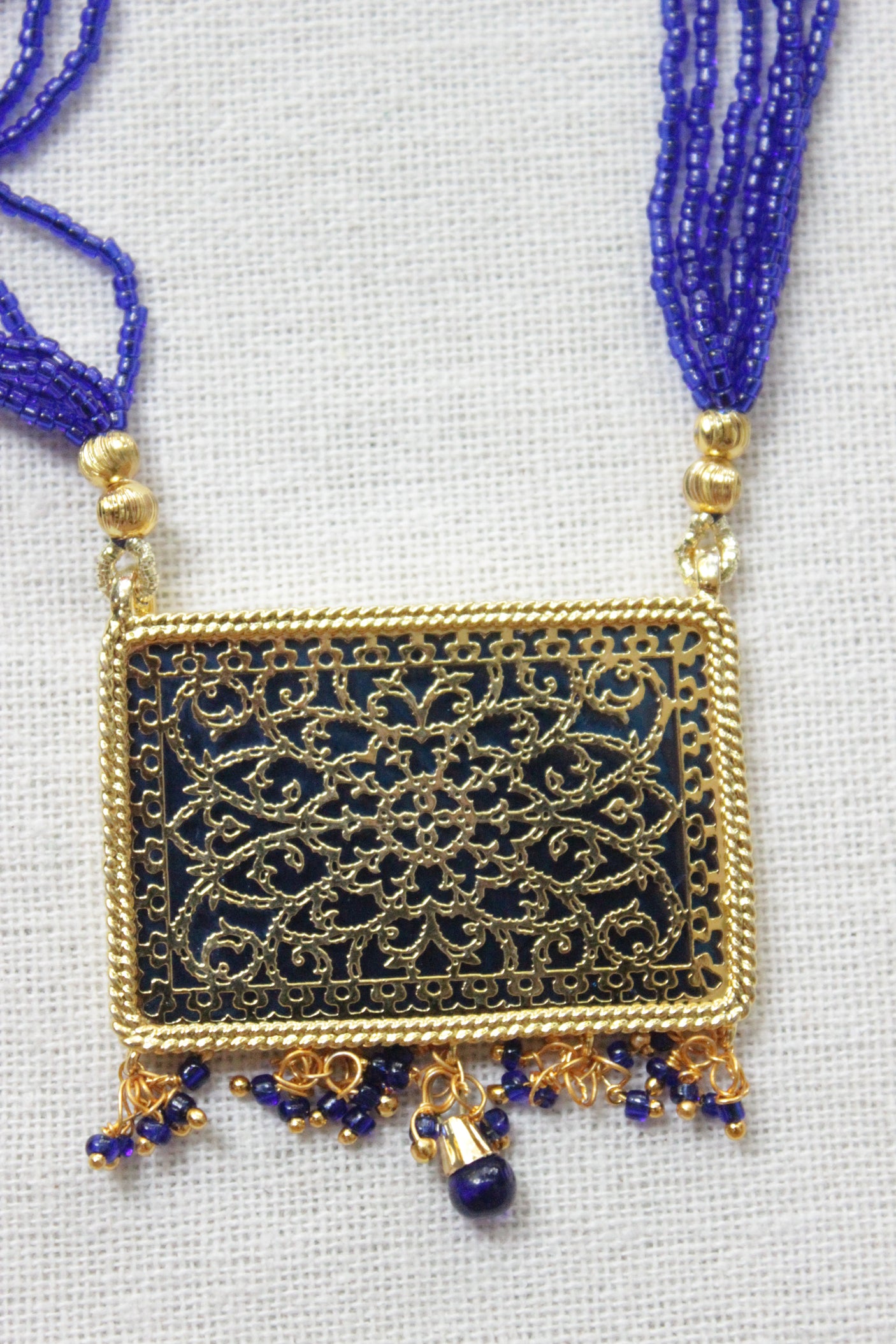 Intricately Detailed Gold Toned Rectangular Pendant Necklace Set with Multi-Layer Blue Beads Closure